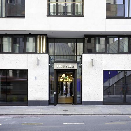 Tower Suites By Blue Orchid London Ngoại thất bức ảnh The image shows the entrance of a modern building, characterized by its minimalist architectural design. The facade features a combination of large glass windows and smooth stone surfaces. The entrance is framed by glass doors, flanked by stylish lig