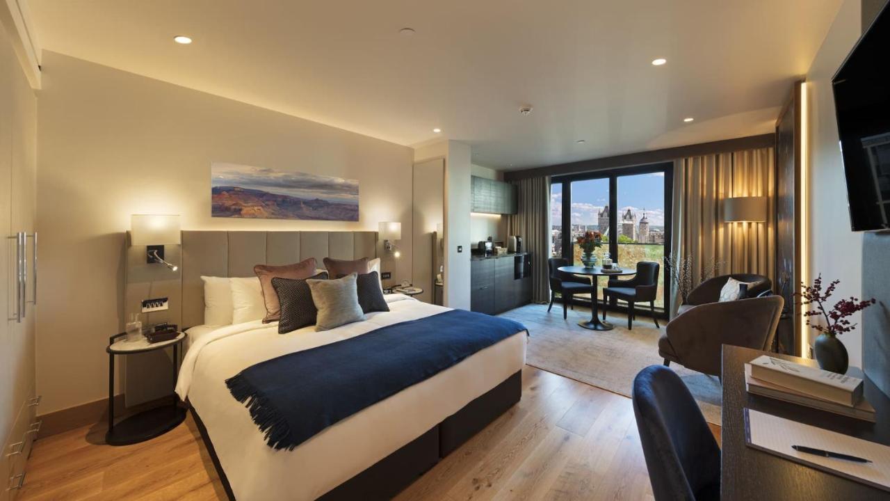 Tower Suites By Blue Orchid London Ngoại thất bức ảnh The photo shows a modern hotel room. It features a large bed with a dark blue throw blanket and several decorative pillows. The walls are painted in neutral tones, and there's a landscape painting above the bed. To one side, there is a small kitchene