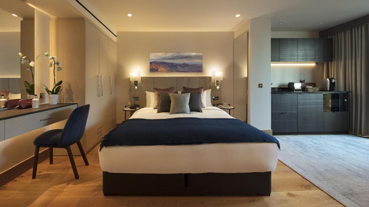 Tower Suites By Blue Orchid London Ngoại thất bức ảnh The photo displays a modern hotel room featuring a plush bed with a dark blue bedspread and several decorative pillows. The walls are adorned in neutral tones, and there is a piece of artwork above the bed depicting a serene landscape. On the side, t