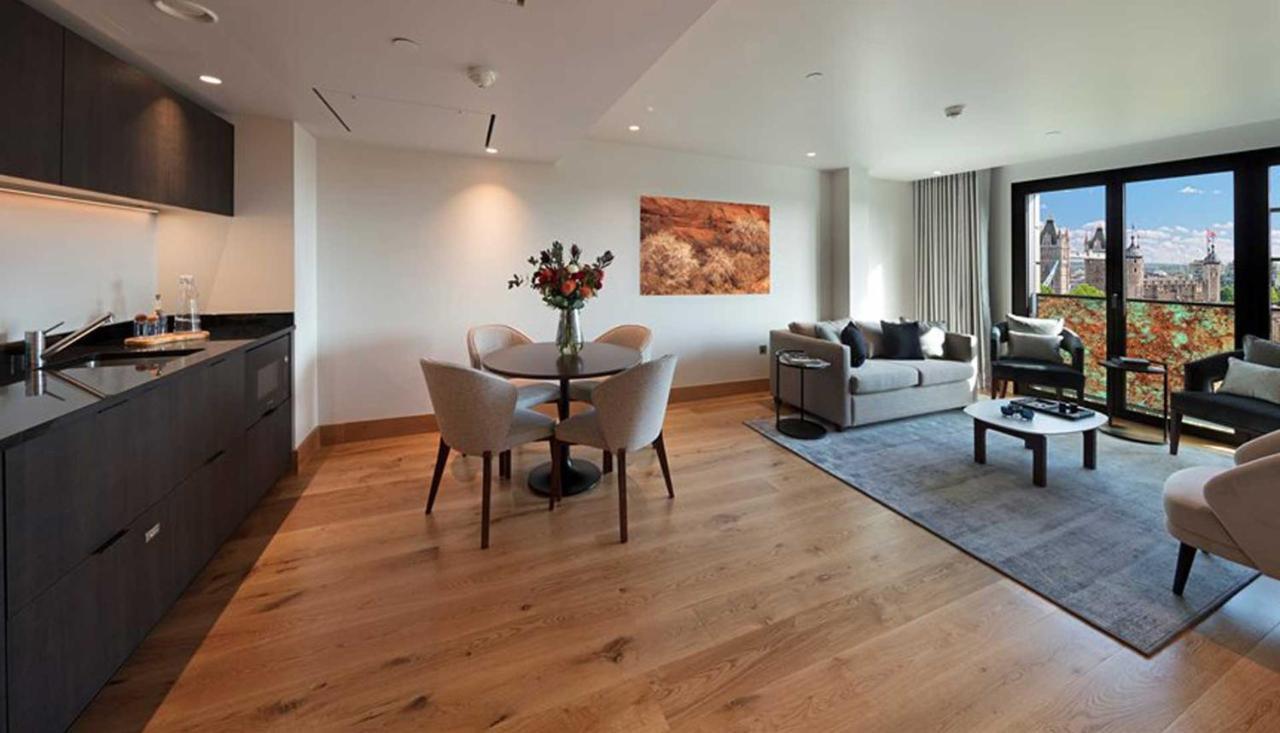 Tower Suites By Blue Orchid London Ngoại thất bức ảnh The photo shows a modern apartment interior. On the left side, there is a kitchen area with dark cabinetry, while on the right side, a comfortable living area is visible. In the center, a round dining table is set with four chairs and a vase of flowe