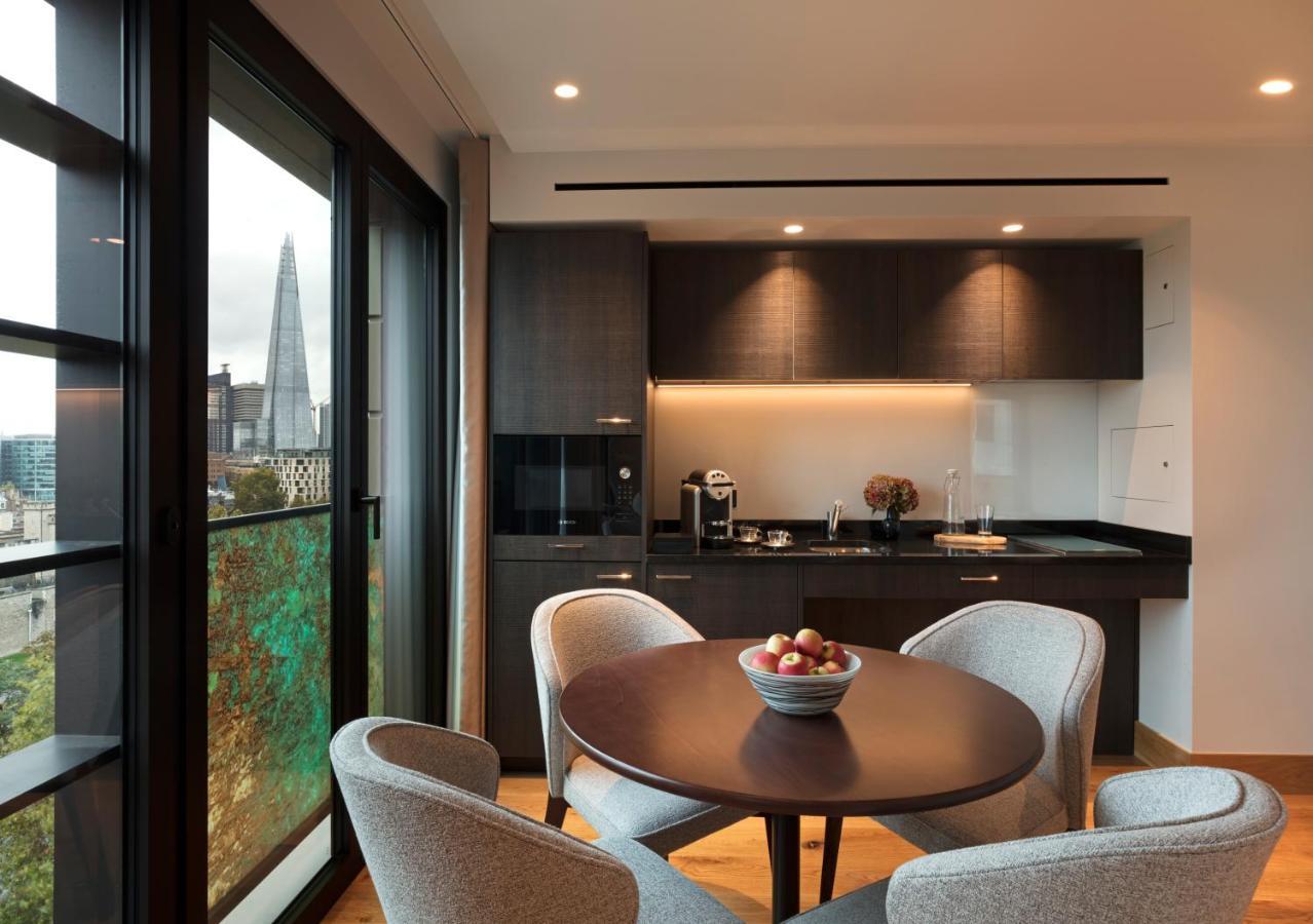 Tower Suites By Blue Orchid London Ngoại thất bức ảnh The photo shows a modern kitchen and dining area. It features a round table with four gray chairs, and a bowl of apples is placed in the center of the table. The kitchen has dark cabinetry, a black countertop, and built-in appliances. Large windows a