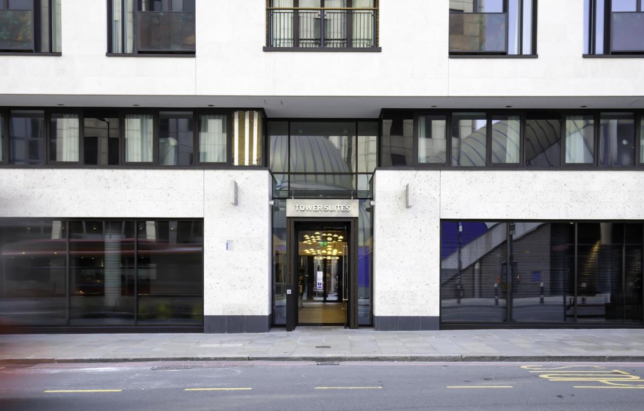 Tower Suites By Blue Orchid London Ngoại thất bức ảnh The image shows the entrance of a modern building, characterized by its minimalist architectural design. The facade features a combination of large glass windows and smooth stone surfaces. The entrance is framed by glass doors, flanked by stylish lig